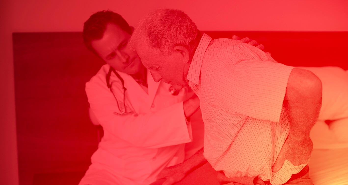 A doctor comforting a man who is holding his lower back from pain